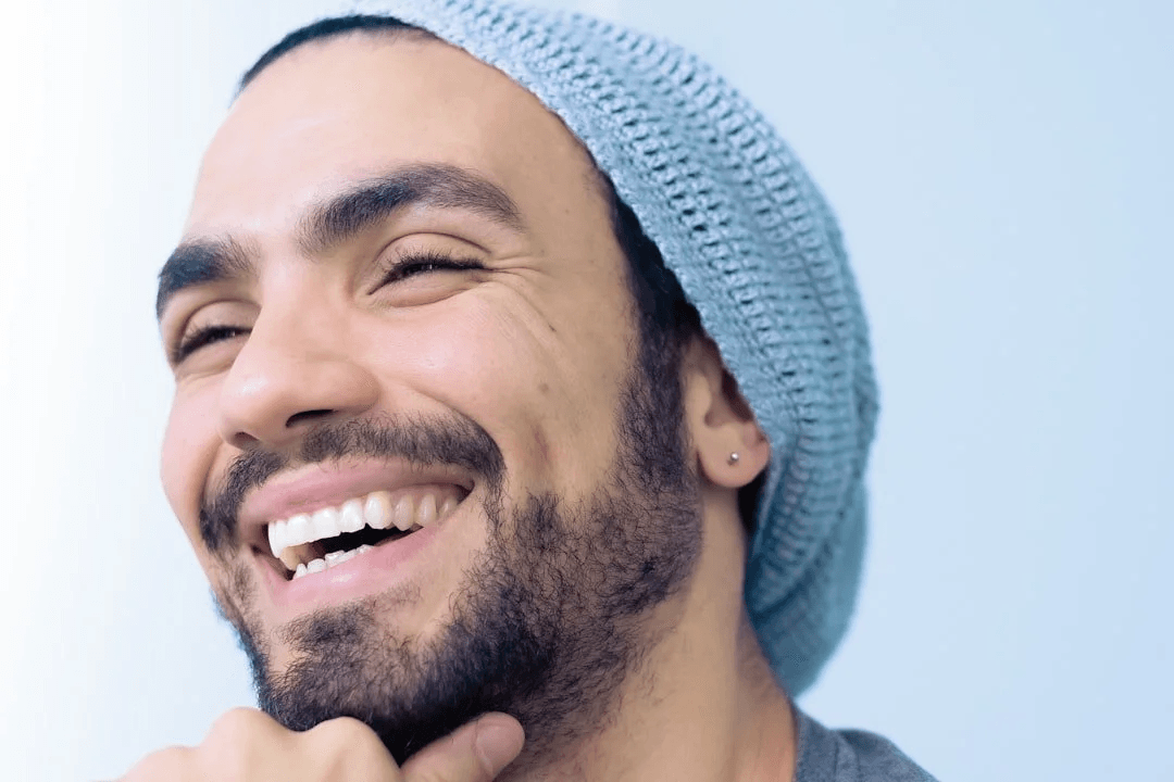 Man in a beanie laughing with a bright, natural smile